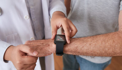 An arm with a black watch on it is being held horizontally, and a hand from another person is adjusting the watch while steadying the watch wearer's hand.